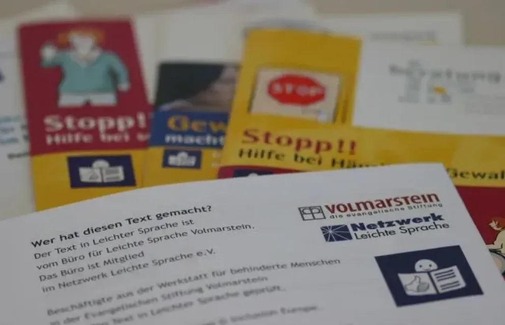 Foto von Texten und Broschüren in Leichter Sprache, mit dem Logo der Evangelischen Stiftung Volmarstein und des Netzwerks Leichte Sprache im Vordergrund.