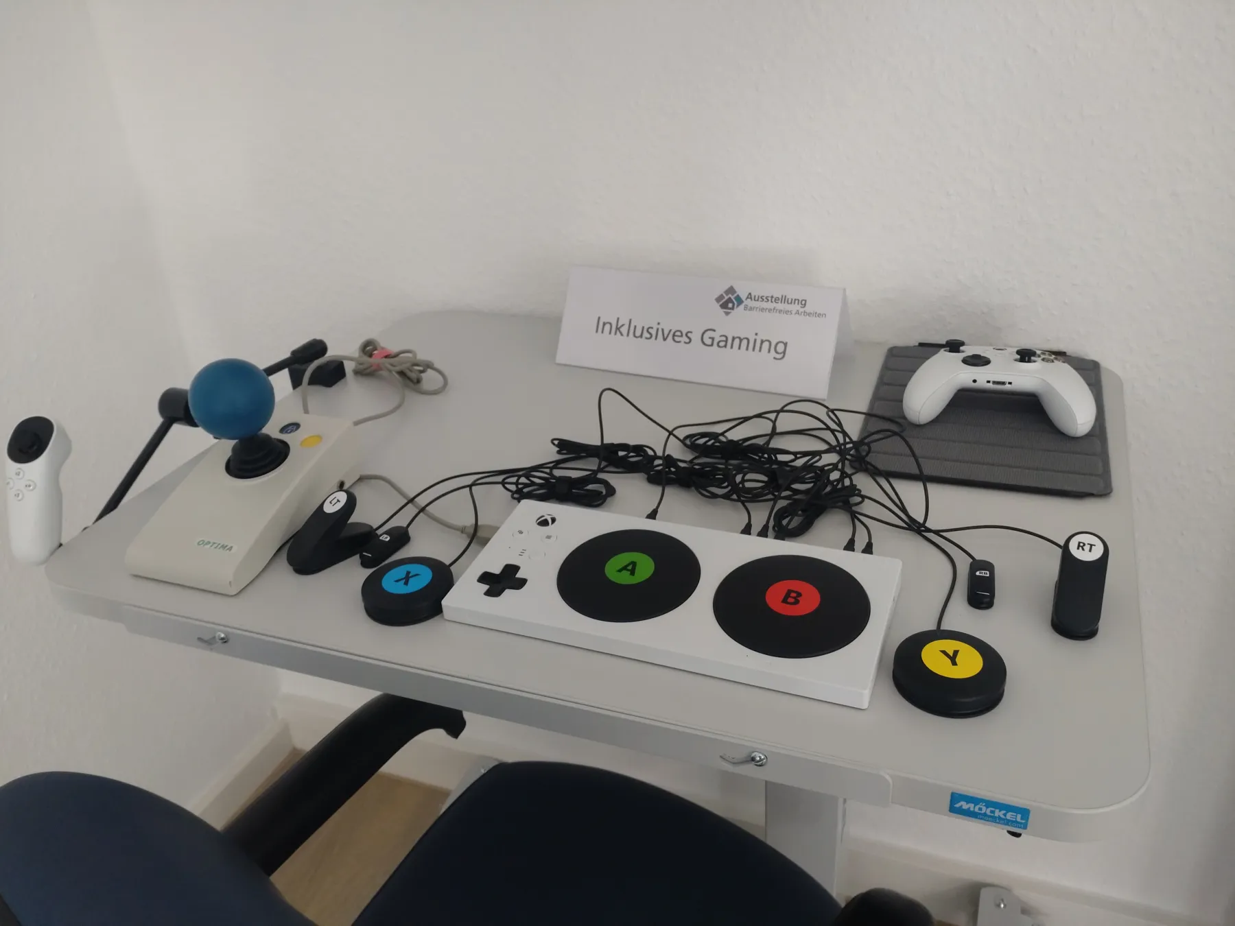 Ein Tisch mit diversen Hilfsmitteln für inklusives Gaming. Ein Joystick, ein Standart-Controller und ein adaptiver Controller mit Tastern von XBOX