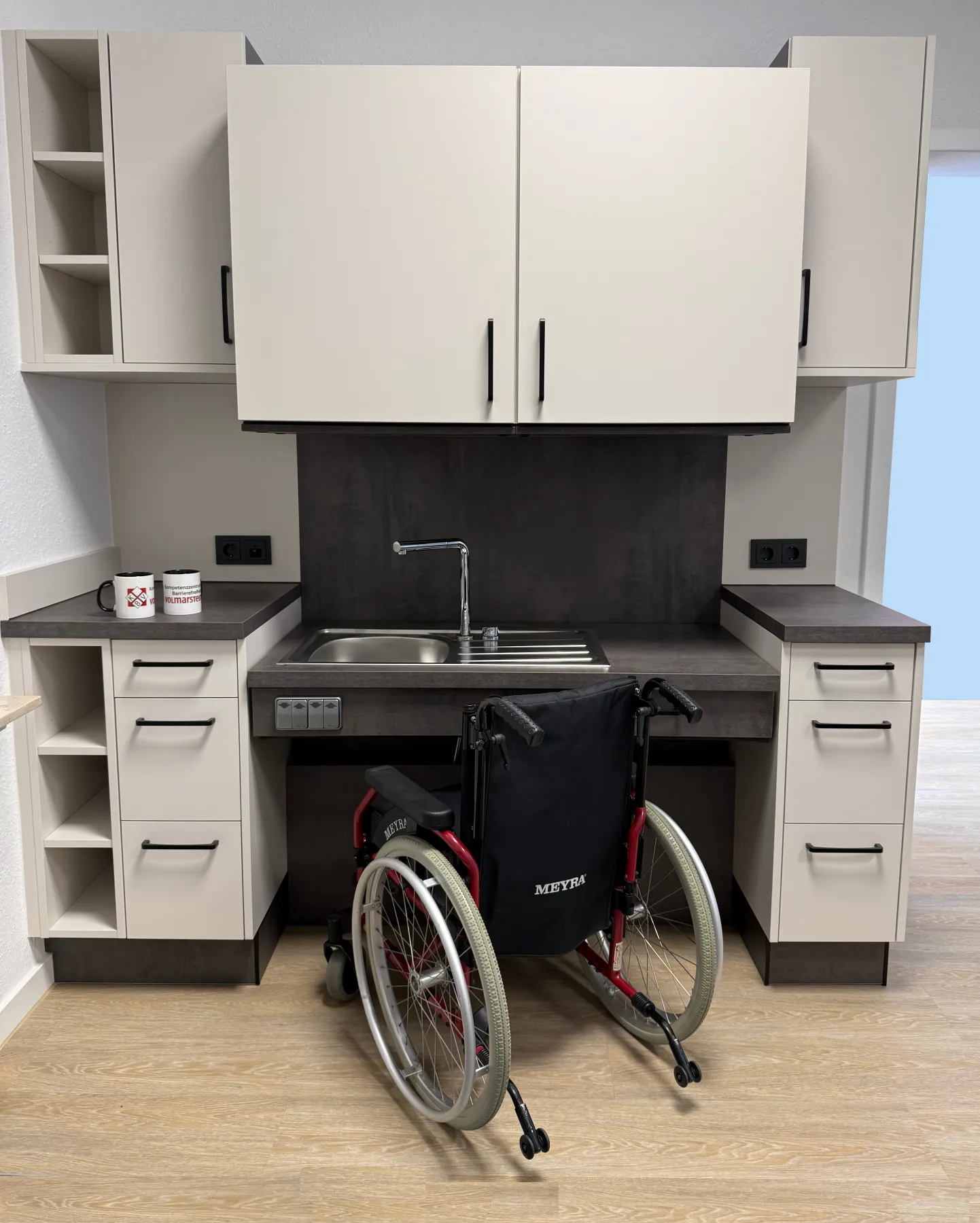 Foto einer rollstuhlgerechten und elektrisch höhenverstellbaren Küche. Der Oberschrank ist abgesenkt.