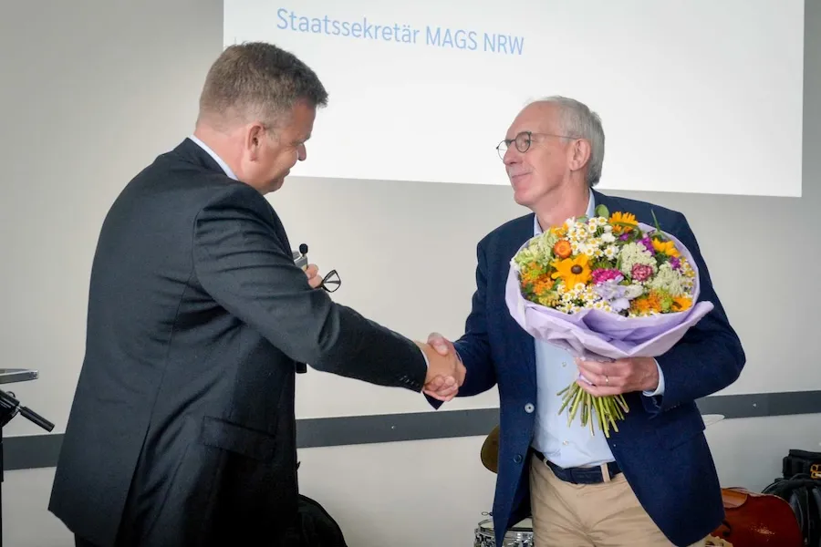 Staatssekretär Matthias Heidmeier verabschiedet Wolfgang Schmitz als Leiter der Agentur Barrierefrei NRW mit einem Straß Blumen