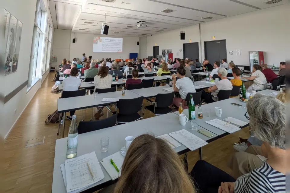 Blick in den Tagungsraum der Fachtagung Wohnberatung mit den von hinten zu sehenden teilnehmenden Wohnberaterinnen und Wohnberatern während eines Vortrags.