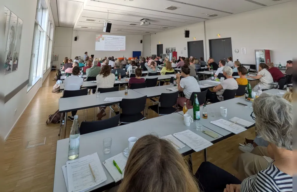 Blick in den Tagungsraum der Fachtagung Wohnberatung mit den von hinten zu sehenden teilnehmenden Wohnberaterinnen und Wohnberatern während eines Vortrags.