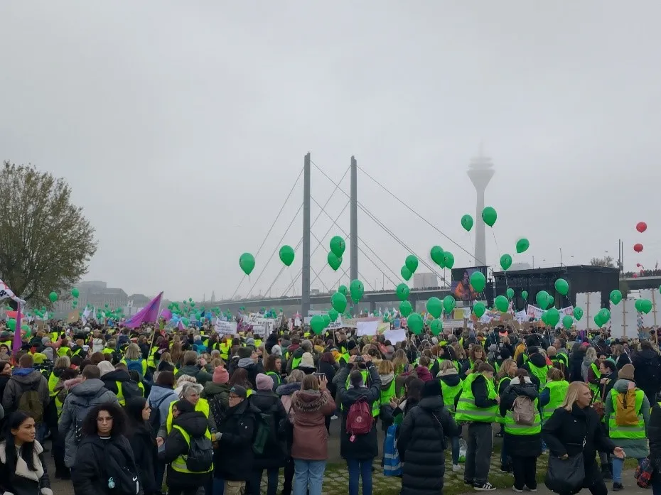Viele Menschen in Warnwesten und mit Luftballons vor einer Bühne im Hintergrund eine Brücke und ein Fernsehturm mit Link zur vergrößerten Ansicht.