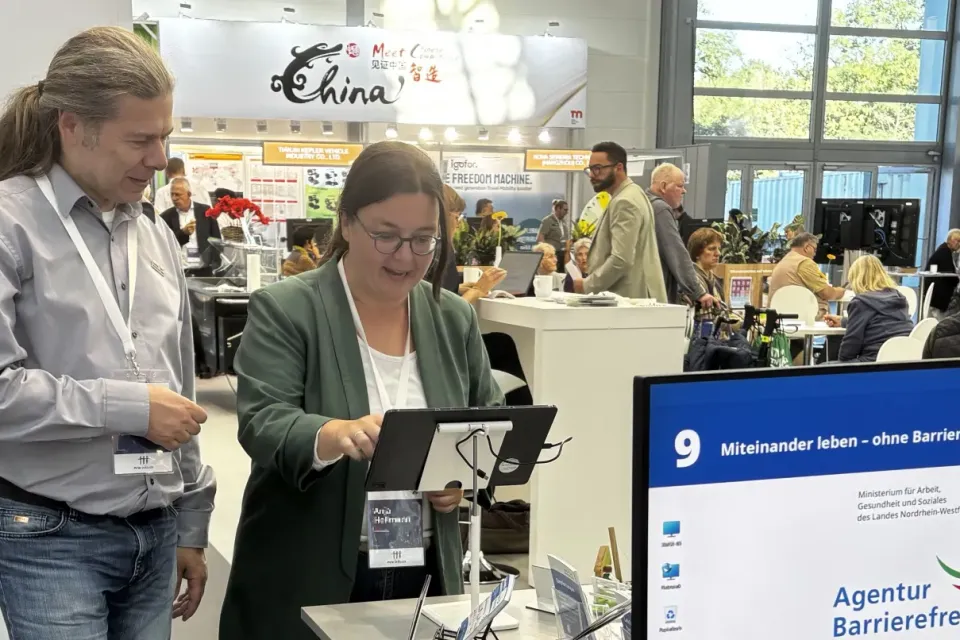 Ein Mitarbeiter der Agentur Barrierefrei NRW erklärt einer Besucherin am Stand das Spiel