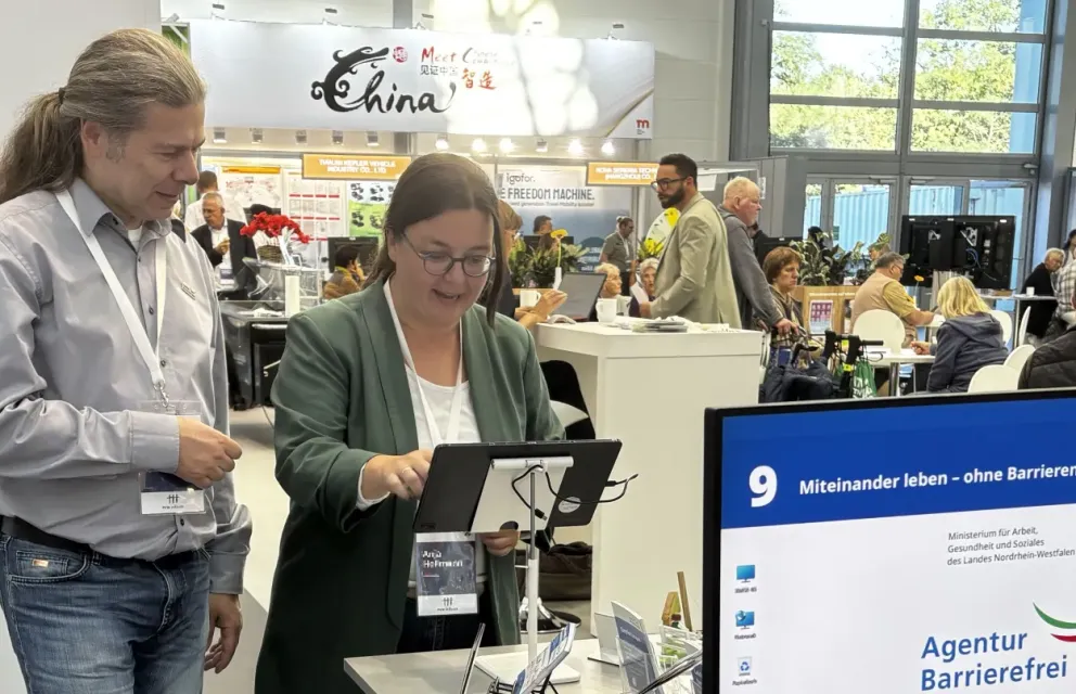Ein Mitarbeiter der Agentur Barrierefrei NRW erklärt einer Besucherin am Stand das Spiel