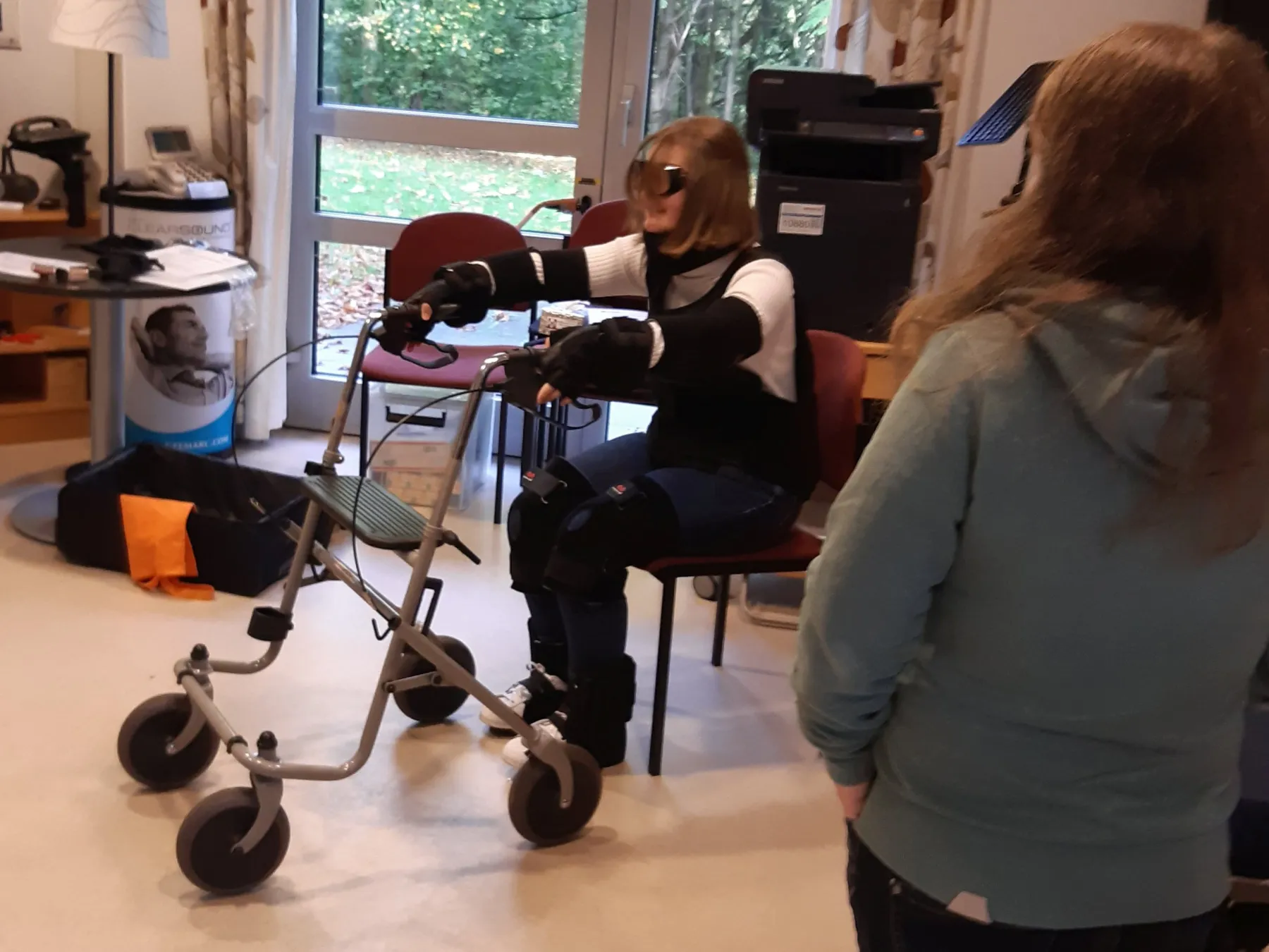 Auszubildende testet im Altersimulationsanzug Hinsetzen und Aufstehen mit dem Rollator.