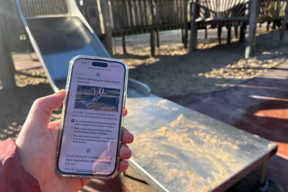 App Spielplatz-Check im Einsatz auf einem Smartphone an einer Rutsche mit langem Ausstieg auf einem Spielplatz