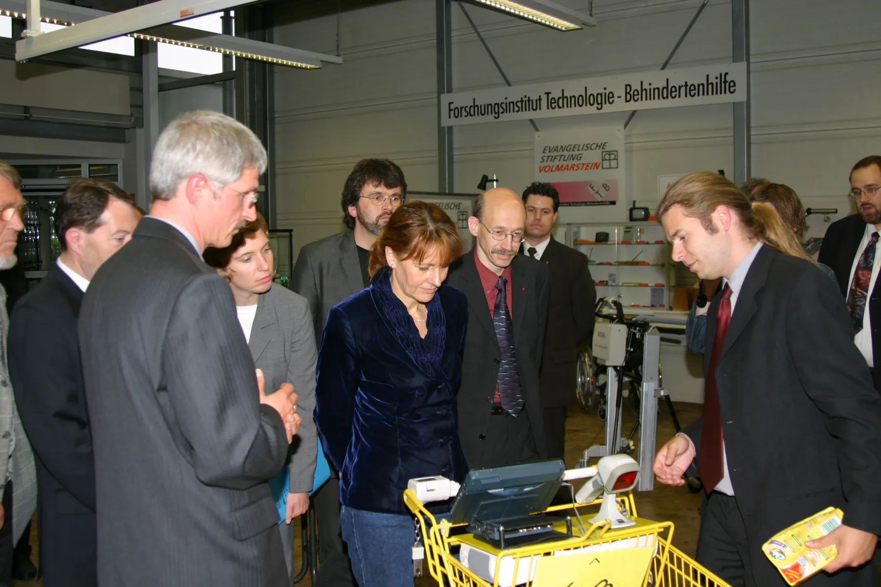 Mitarbeitende des FTB demonstrieren Ministerin Buhlman eine Entwicklung, die in Form eines Displays und Scanners an einem Einkaufswagen montiert ist.