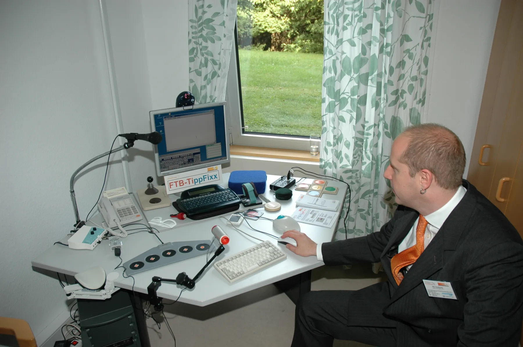 Demonstration von FTB-Tippfixx in der Demonstrationswohnung durch einen FTB-Mitarbeiter an einem mit Hilfsmitteln ausgestatteten Computerarbeitsplatz.