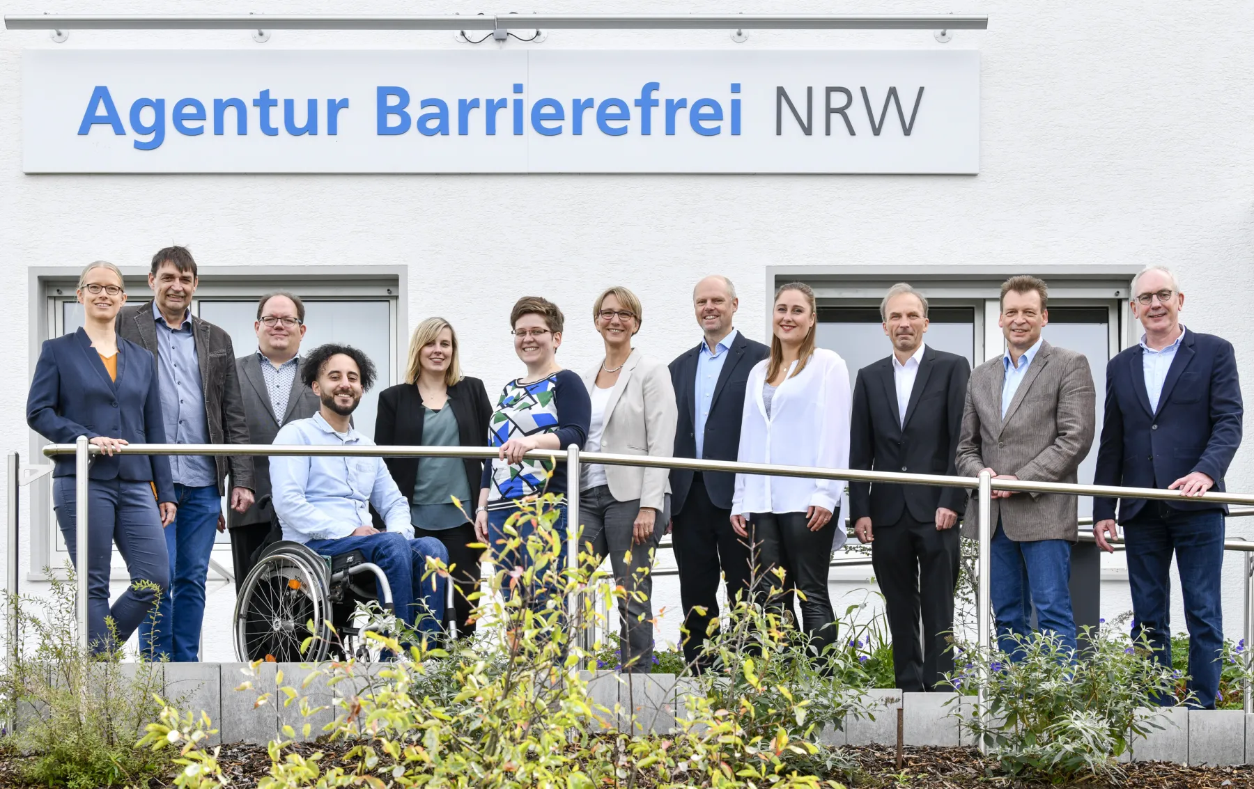 Foto von 12 Mitarbeitenden des Agenturteams vor dem Gebäude der Agentur Barrierefrei NRW.