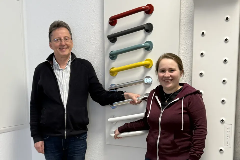 Foto von den Wohnberatern Hans-Werner Geburek und Hanja Laumann vor einer Wand mit verschiedenfarbigen Haltegriffen
