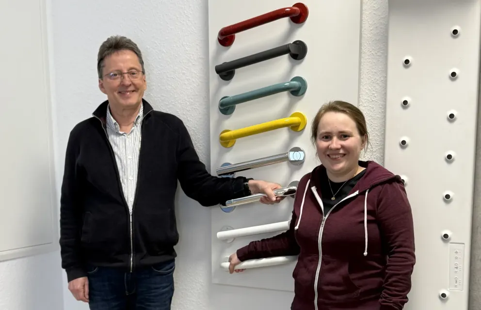Foto von den Wohnberatern Hans-Werner Geburek und Hanja Laumann vor einer Wand mit verschiedenfarbigen Haltegriffen
