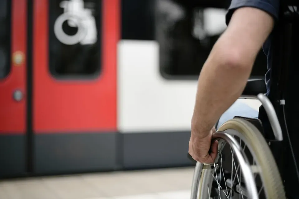 Rollstuhlfahrer am Bahnsteig auf dem Weg zu einer mit einem Rollstuhl-Symbol gekennzeichneten Tür eines Regionalzugs.