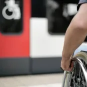 Rollstuhlfahrer am Bahnsteig auf dem Weg zu einer mit einem Rollstuhl-Symbol gekennzeichneten Tür eines Regionalzugs.