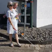 Zwei Frauen laufen eine Rampe runter. Eine Frau hat eine Augenbinde, wodurch die blind ist und hat einen Langstock in der Hand. Die andere Frau sichert sie ab.